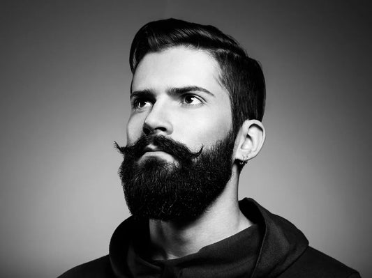 Homem com bigode estilizado de pontas curvadas e barba escura, close em preto e branco
